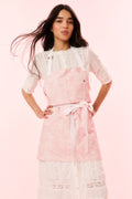 Perennial pink printed apron with white lace bib and waist tie, worn over white