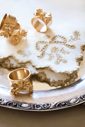 White dinner napkins set with gold embroidered ribbon bows and scalloped trim