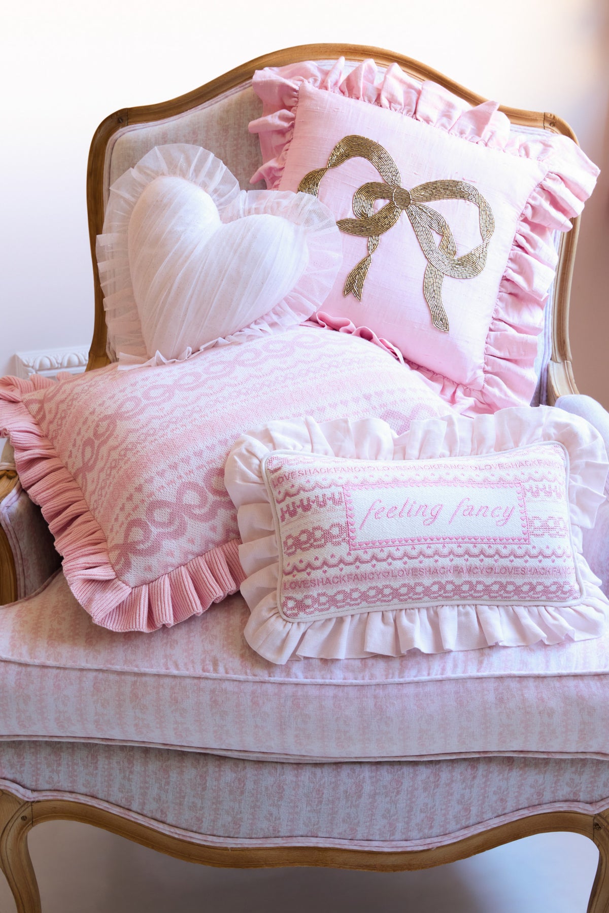 Pink decorative needlepoint pillow with ruffled trim, gold bow and heart design