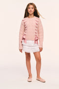 Tween pink textured knit pullover with ribbon threaded through the sides and bow at hem paired with a white mini skirt
