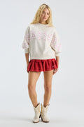 Cream mockneck crew sweatshirt with “LOVE” applique; styled with red tutu skirt