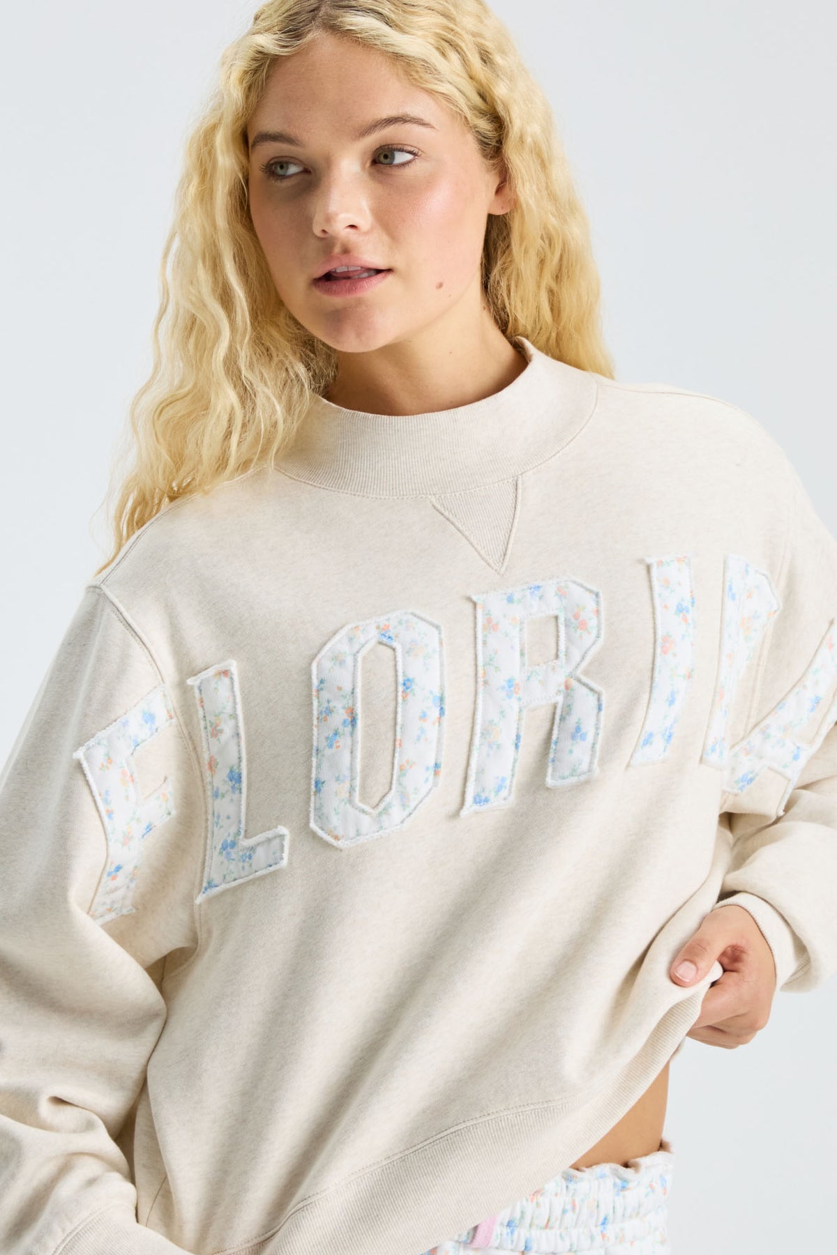 Cream mockneck crew sweatshirt close-up with pastel “LOVE” applique detail
