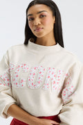 Close-up of cream mockneck crew with “FANATICS” lettering and pink floral print