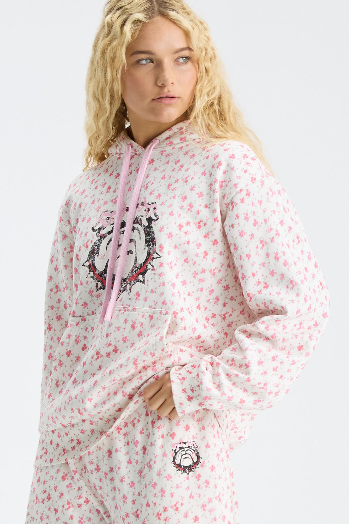 Pink floral-print hoodie with hood and drawstring, front logo graphic partially visible