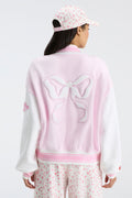 Light pink varsity jacket back with bow emblem and ribbed striped collar and hem.