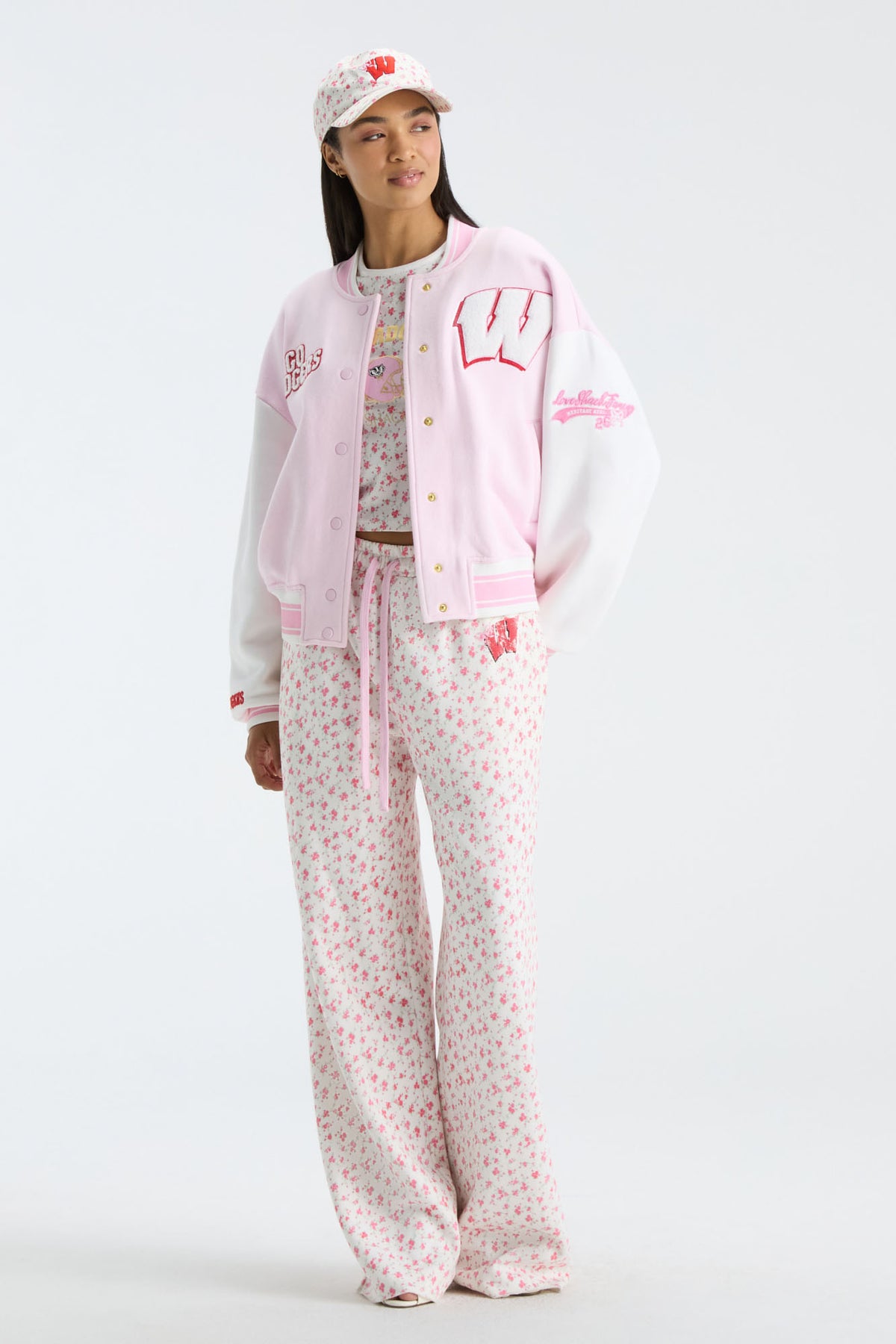 Light pink varsity jacket with patches worn with floral pants and a patterned cap.