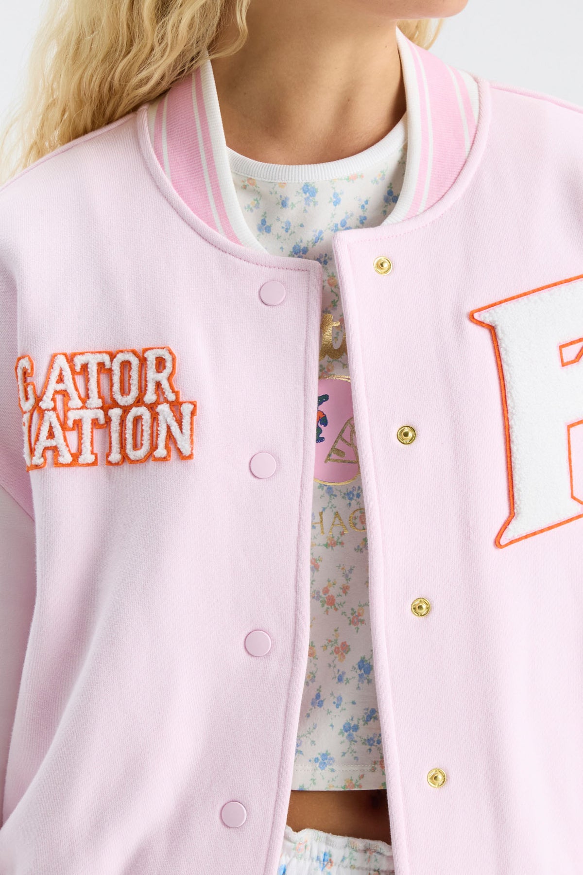 Close-up: pink varsity jacket front with embroidered orange text and “A” patch