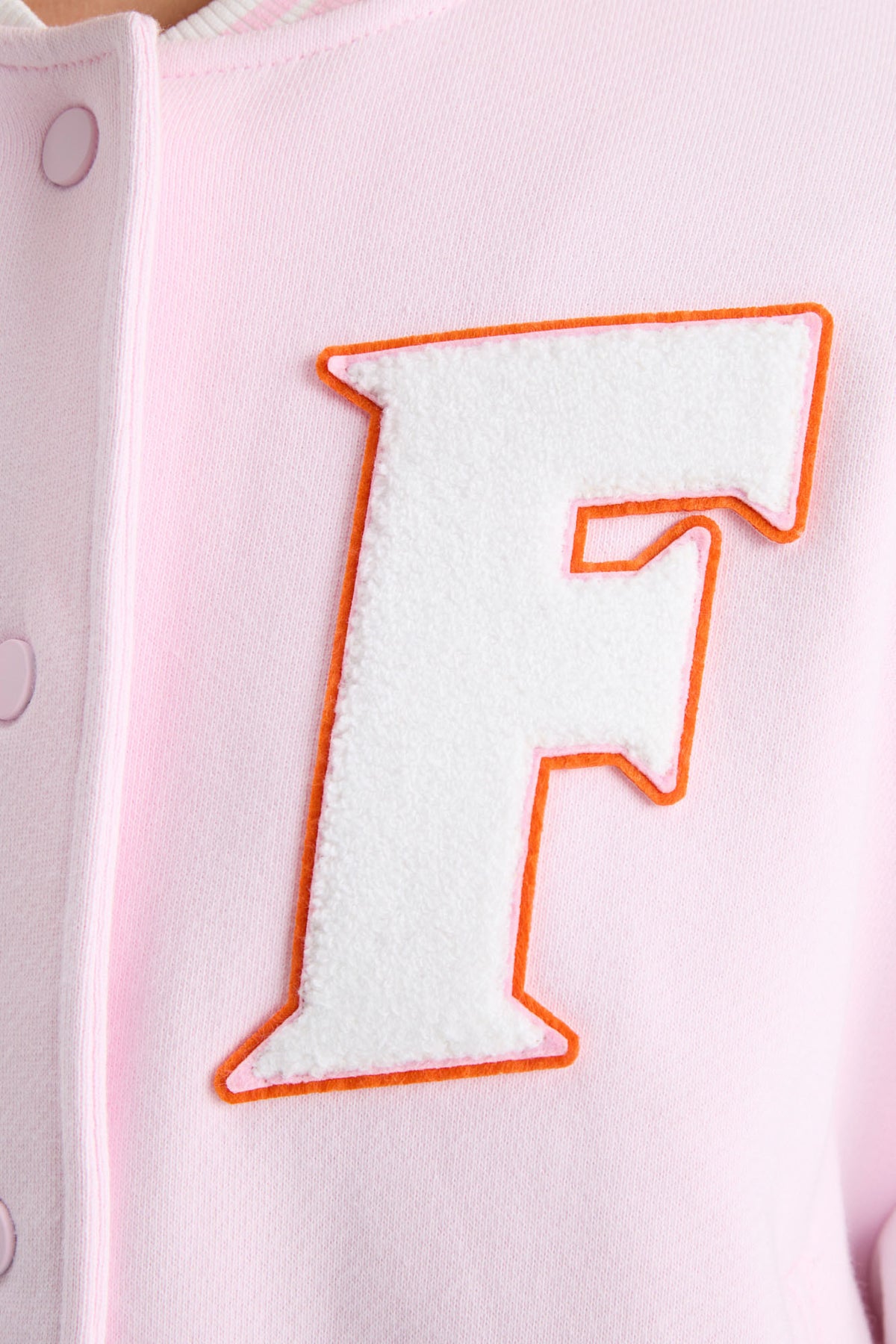 Close-up of embroidered orange “F” on light pink varsity jacket