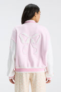 Pink varsity jacket with white sleeves and large bow graphic on the back.