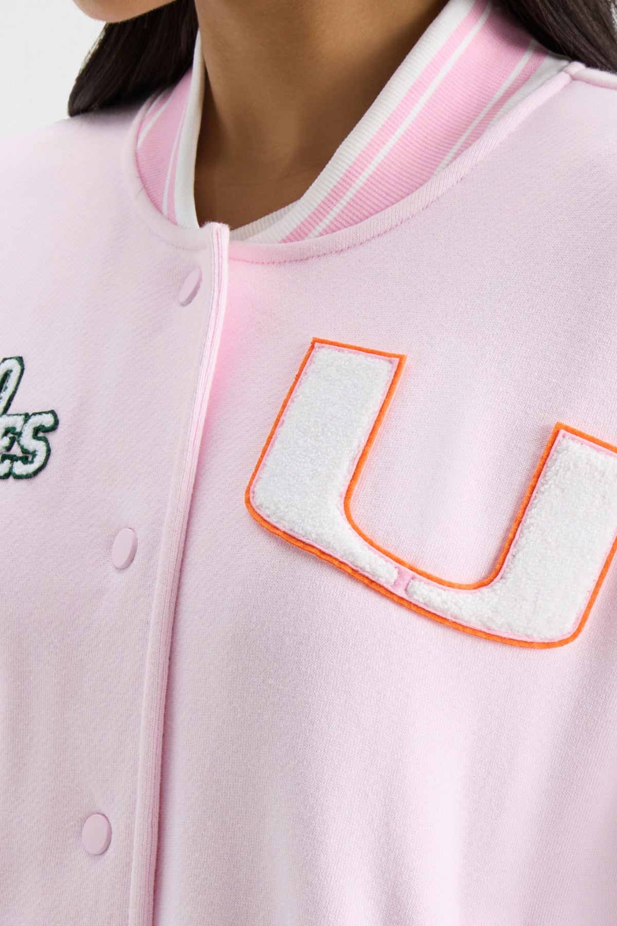 Light pink varsity jacket close-up with ribbed collar and orange-outlined T patch