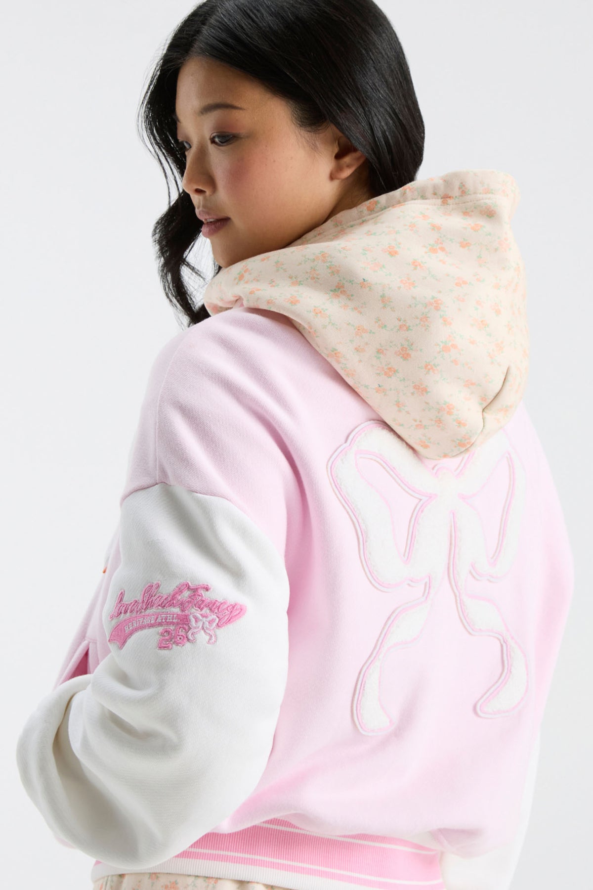 Pink varsity jacket with raised bow applique and striped ribbed cuffs on a model