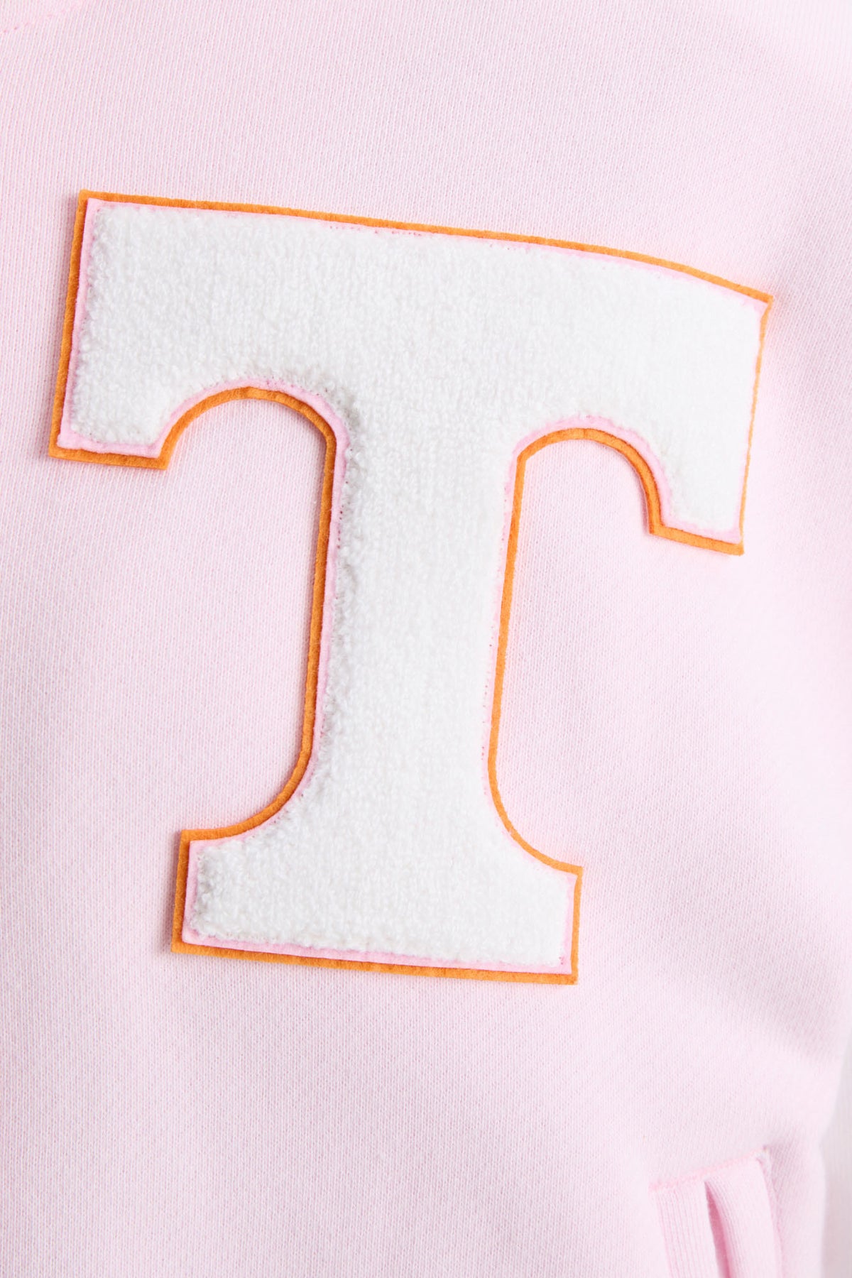 Close-up of orange-outlined T letter patch on pink varsity jacket