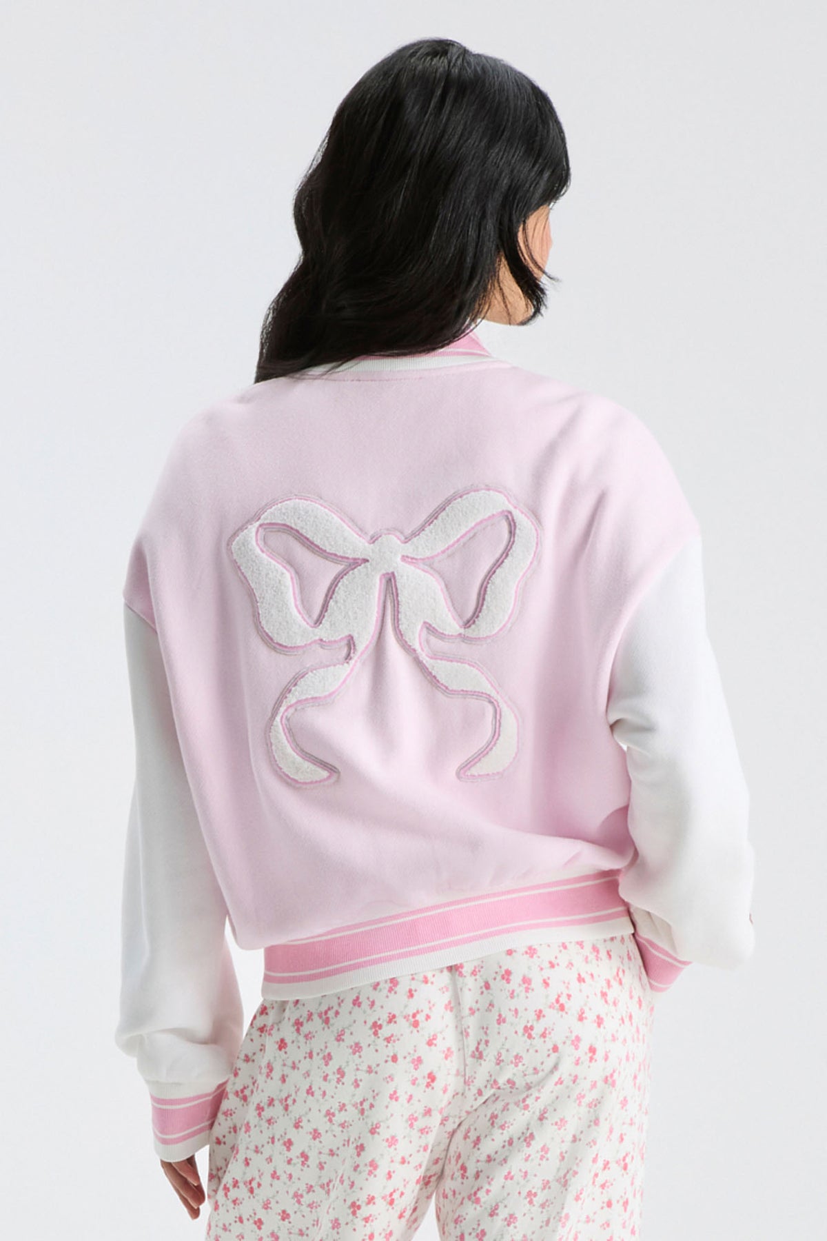 Light pink varsity jacket back with bow applique and ribbed striped waistband trim.