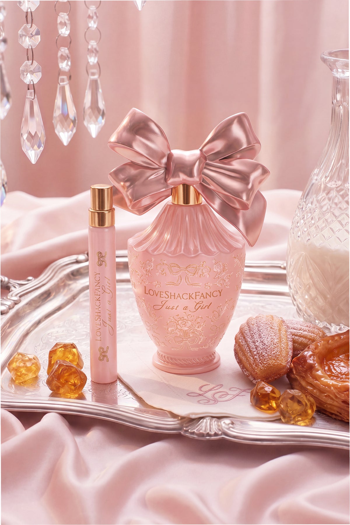 Pink bow perfume bottle with gold cap, shown on a tray with small gold candies