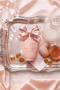 Pink bow perfume bottle on ornate tray with ribbon detail and amber-colored crystals