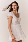 White cotton Victorian mini dress on model, V-neck, embroidered yoke, lace hem