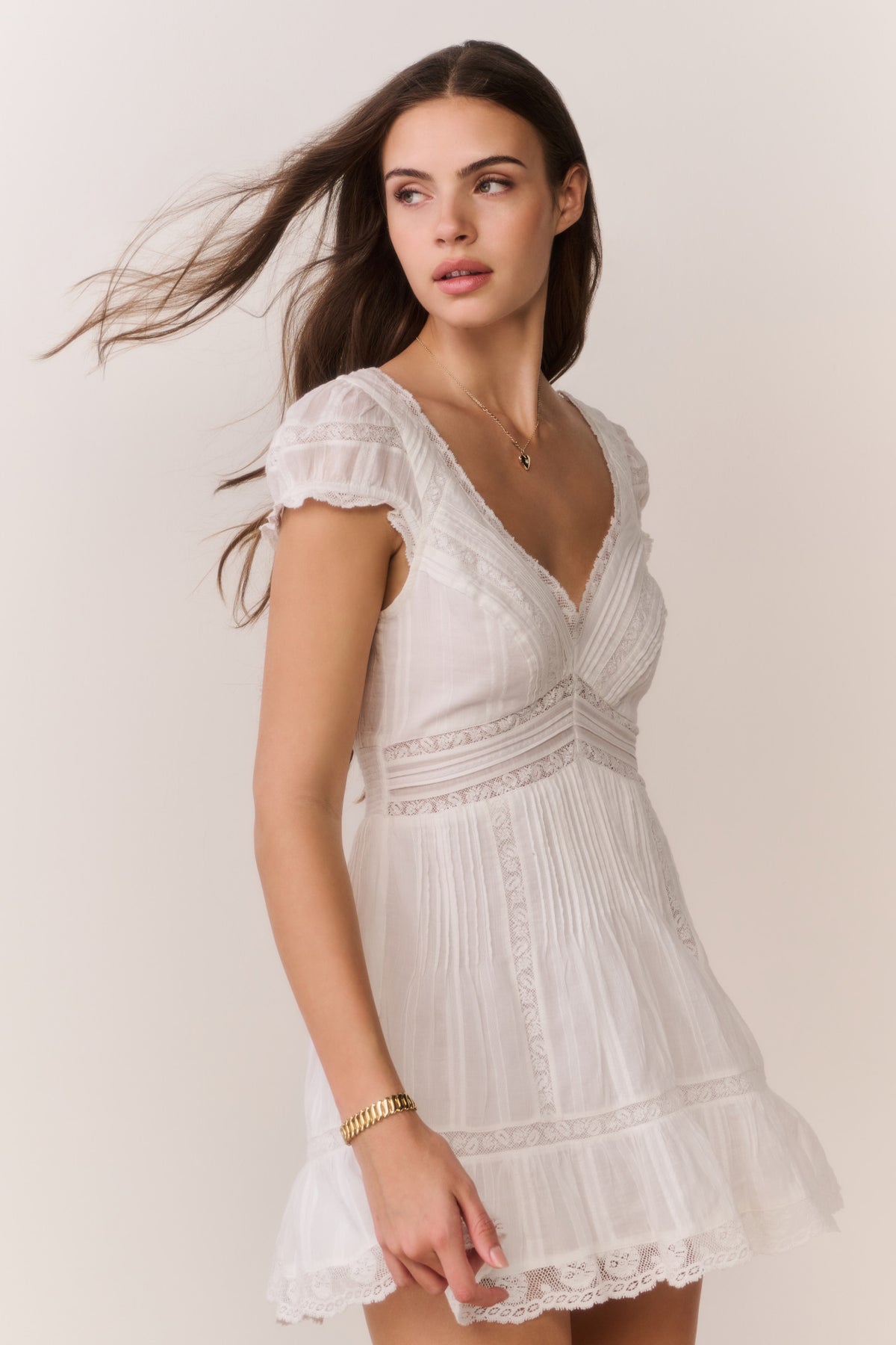 White cotton Victorian mini dress on model, V-neck, embroidered yoke, lace hem