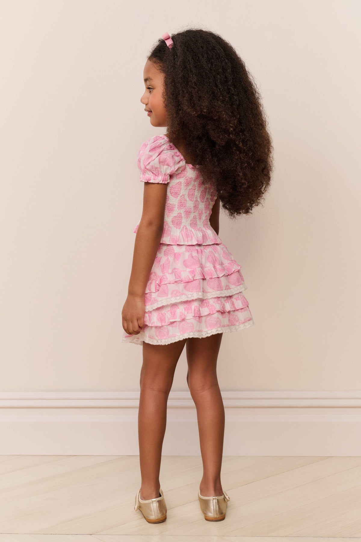 Girls pink heart-print top in side profile with puff sleeves and layered ruffle hem
