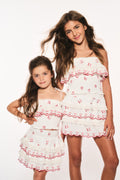 Girls' white cotton cherry print ruffle cami top with red trim, worn front view