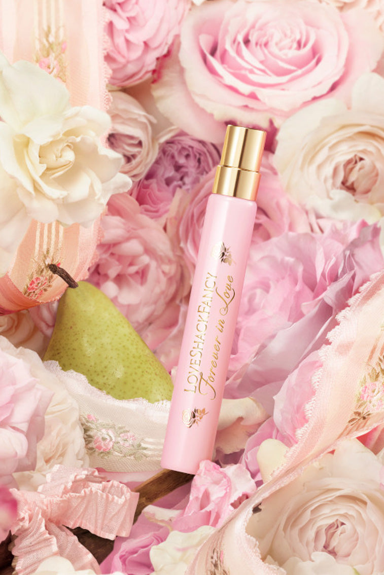 Pink eau de parfum travel spray with gold cap in a floral setting