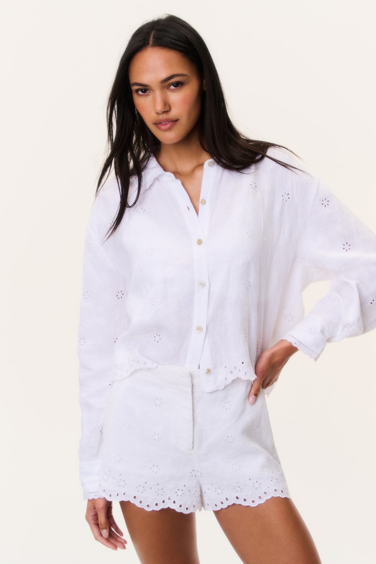 White eyelet button-up top with V-neck placket, long sleeves, scalloped hem.