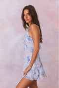 Silk mini dress with blue floral print and spaghetti straps, side view with ruffle hem.