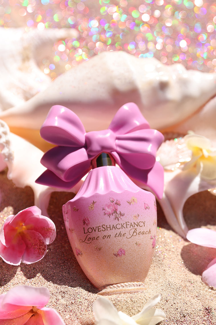 Pink Love on the Beach eau de parfum bottle with oversized bow on sandy beach