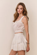 White eyelet crop top with lace scalloped neckline, sleeveless ruffles, and button placket