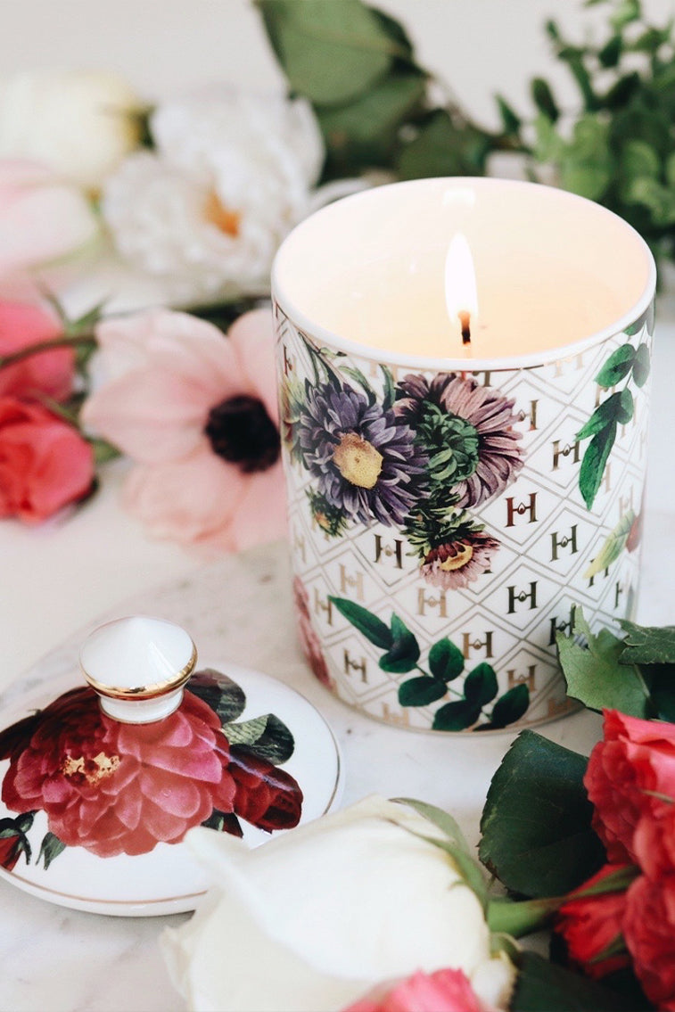 Burning candle in white floral ceramic jar with gold-trimmed lid