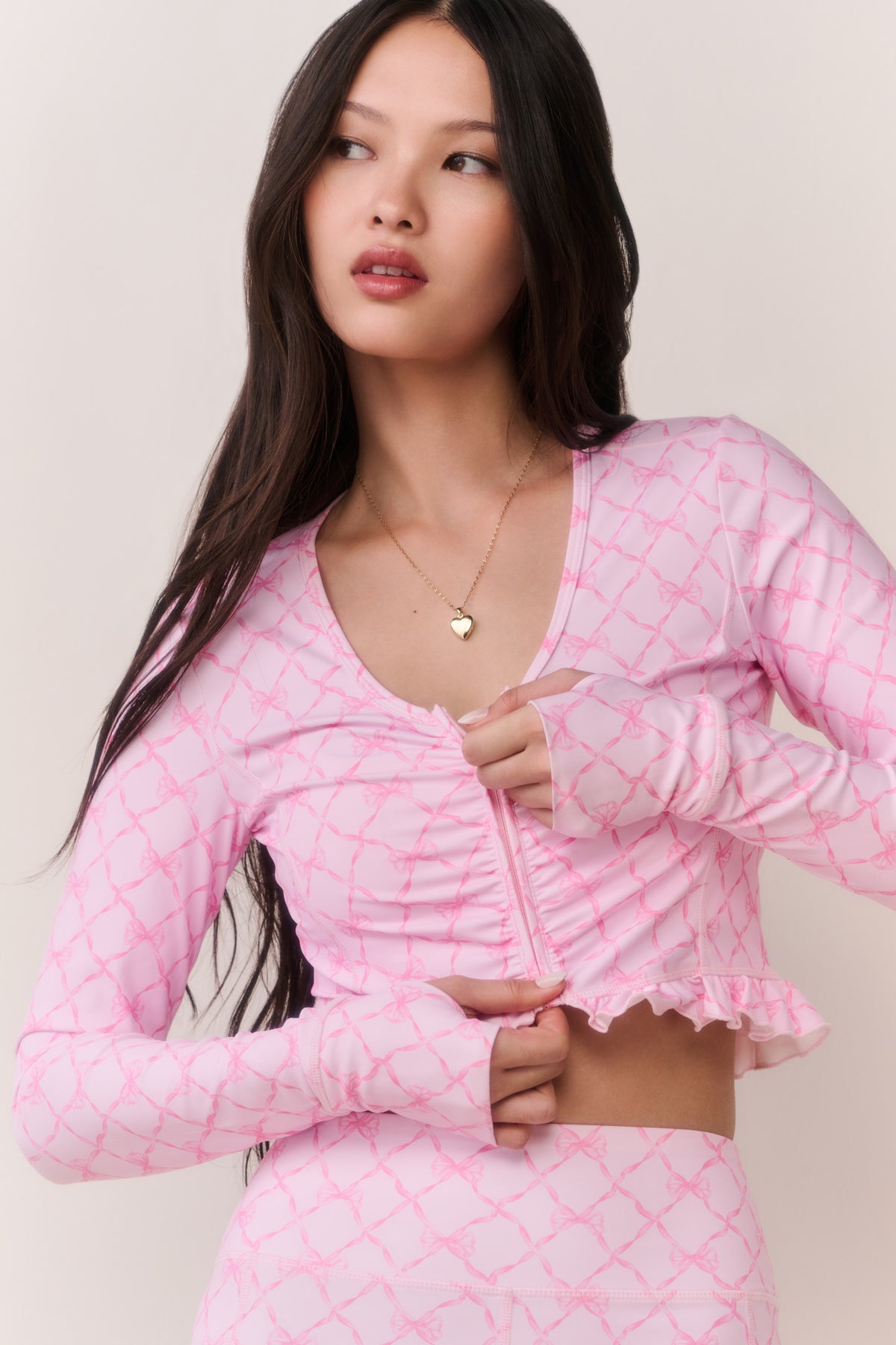 Pink printed zip-up active top with V-neck, long sleeves, front zipper, and ruffle trim