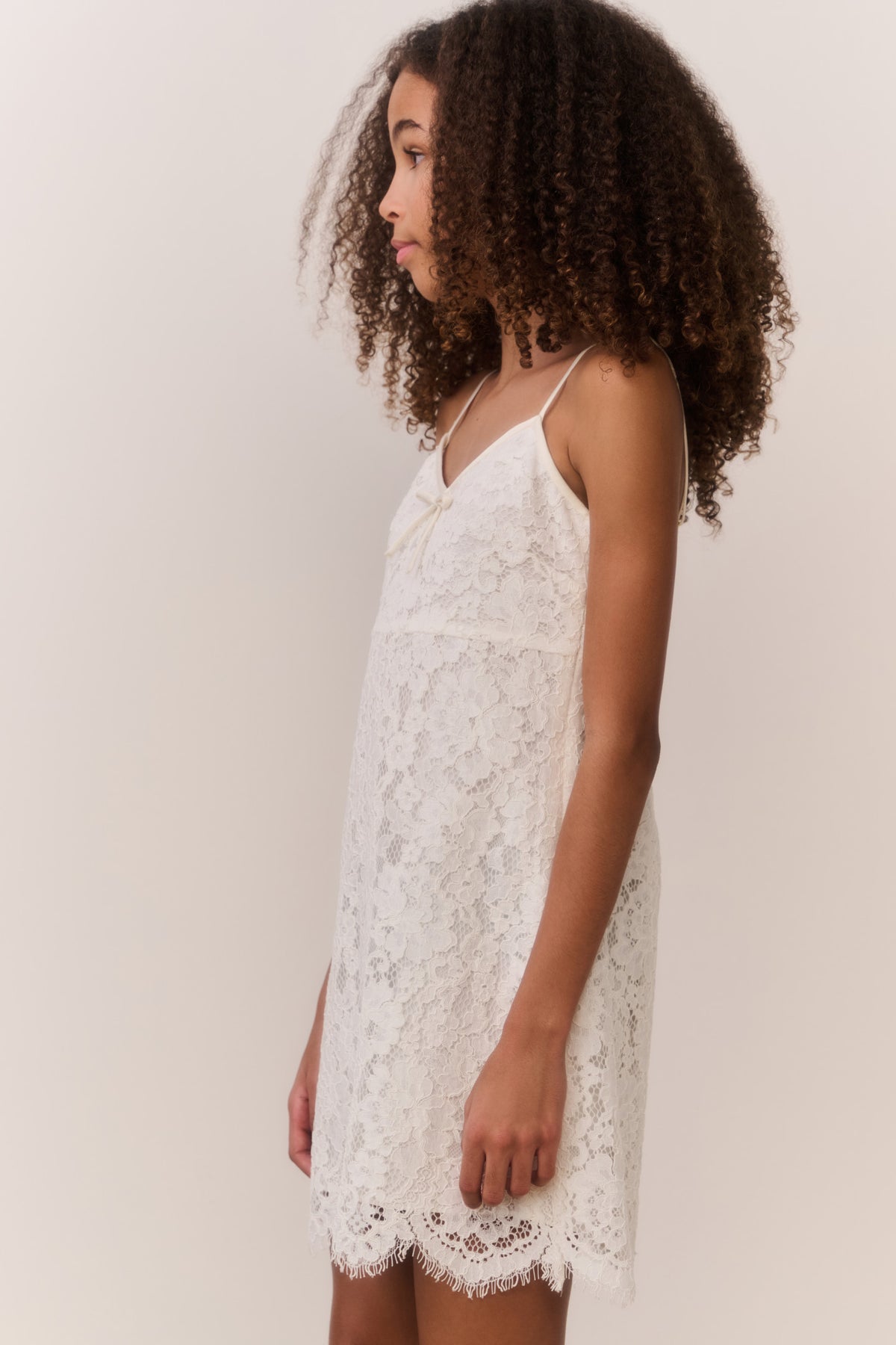 Ivory lace mini dress with spaghetti straps and scalloped hem, side view