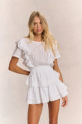 White mini dress with ruffled sleeves, smocked waist, and tiered ruffle skirt