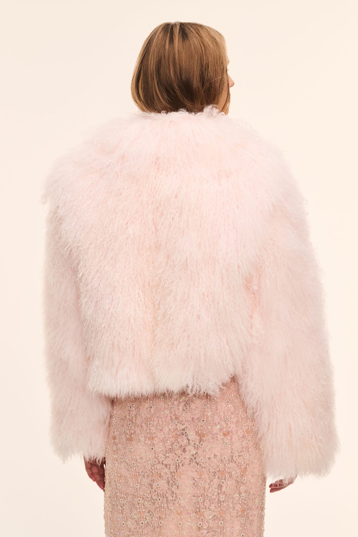 Back view of pale pink fluffy shearling jacket, long sleeves and cropped length