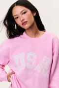 Pink fleece pullover, close-up of chest "USA" print with small decorative dots.