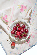 Floral patchwork table linen with pink and blue stitched corners and fringed hem.
