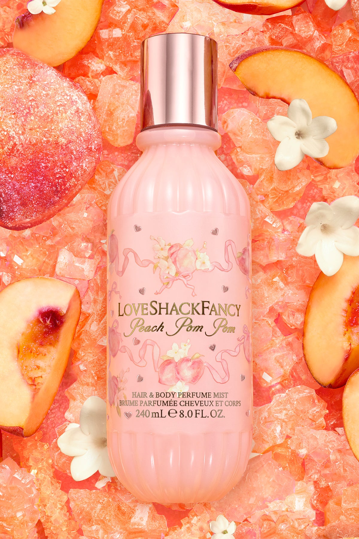 Pink hair and body perfume mist bottle with pump, surrounded by fruit and flowers