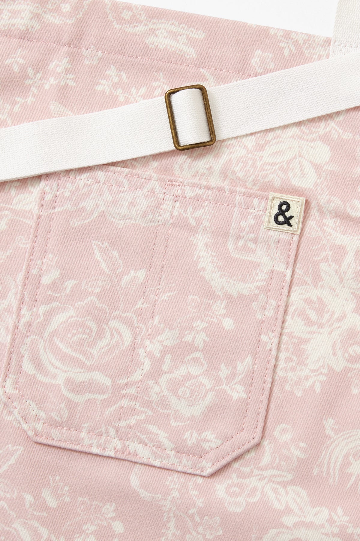 Close-up of pink apron with white strap, square buckle, and small logo patch