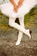 Bone cowboy boots with embossed scroll stitching and pointed toe, shown on the wearer