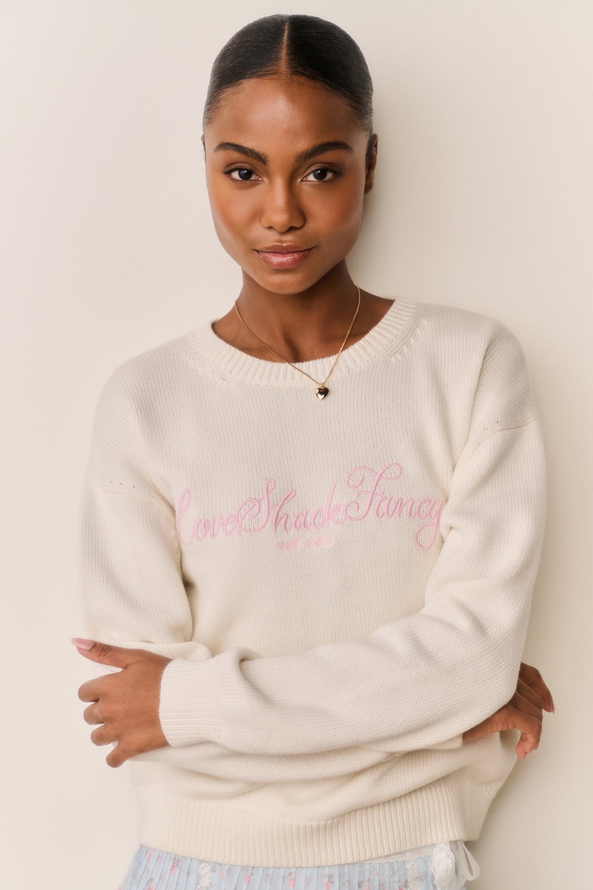 Cream cotton pullover with ribbed crew neck, long sleeves, and pink embroidered text