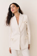 Cream wool-blend blazer with bow embellishments on lapel, cuffs, and flap pockets, close-up
