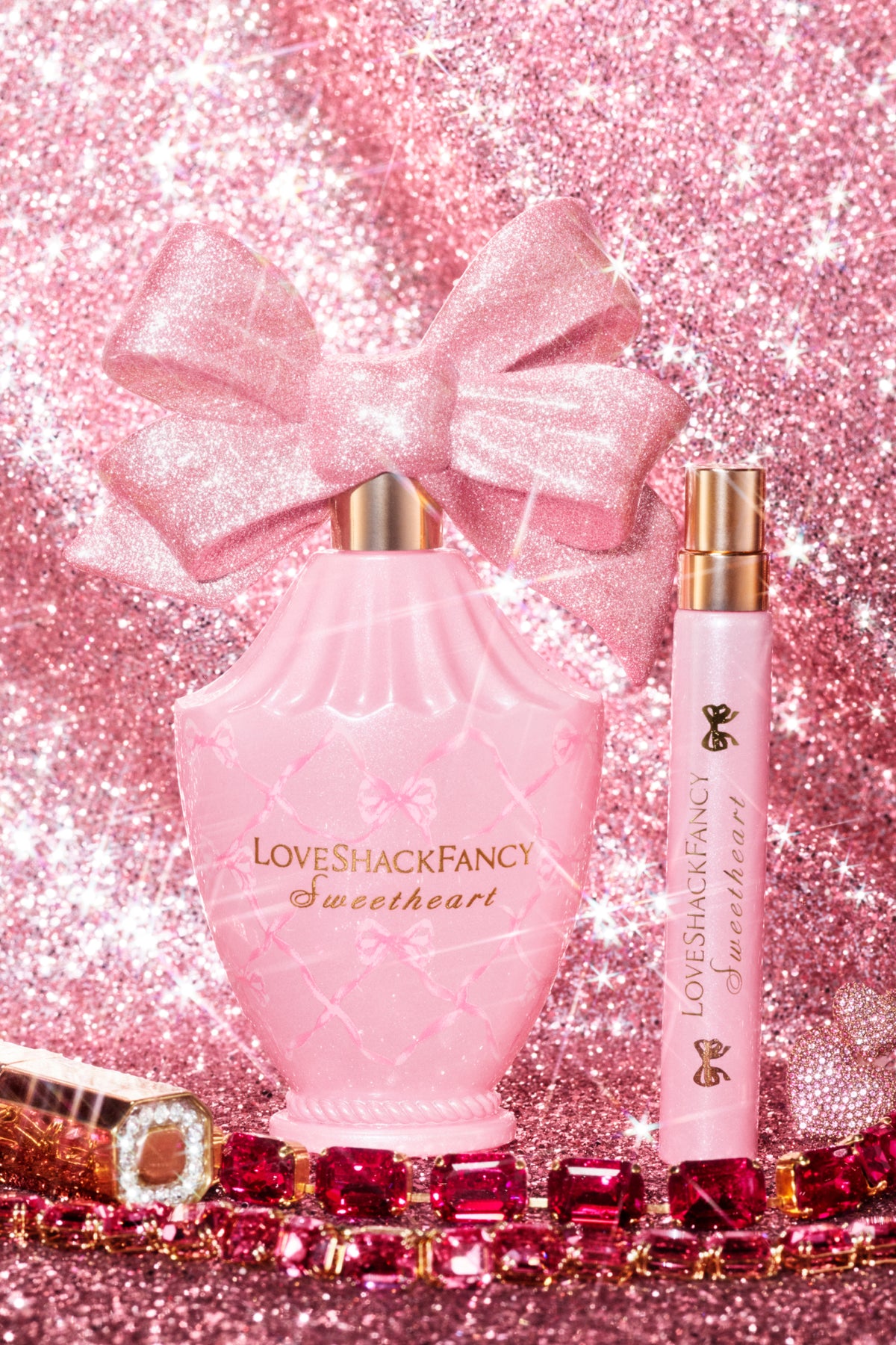 Pink perfume bottle with bow and two matching travel spray bottles with gold caps.