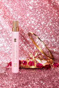 Pink Loveshack travel perfume spray bottle with gold cap, on glittery pink surface.