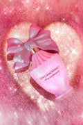 Pink perfume bottle with large pink bow and gold cap, surrounded by glittery heart.