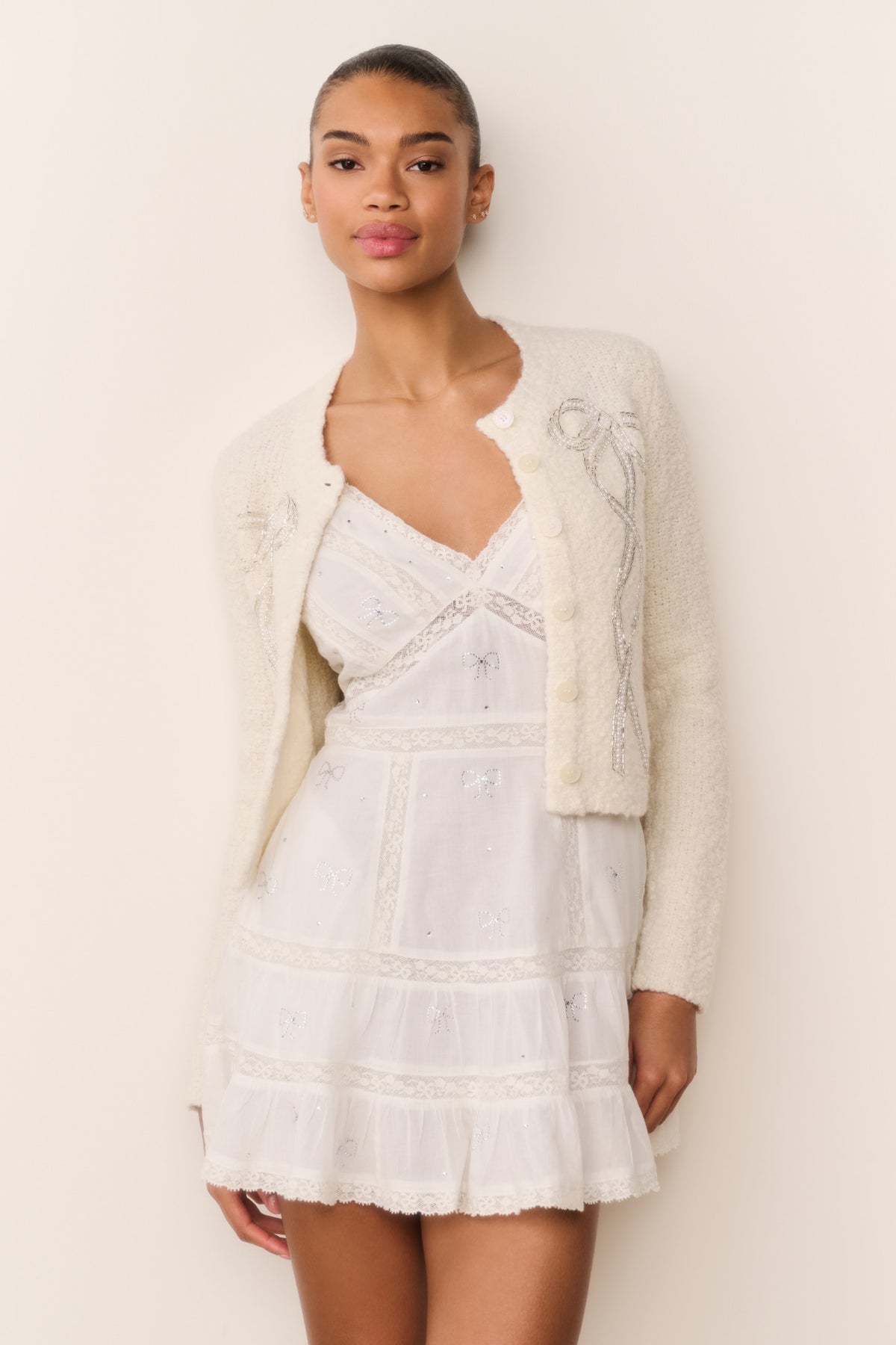 White cotton mini dress with spaghetti straps and tiered ruffle skirt, bow motif detail
