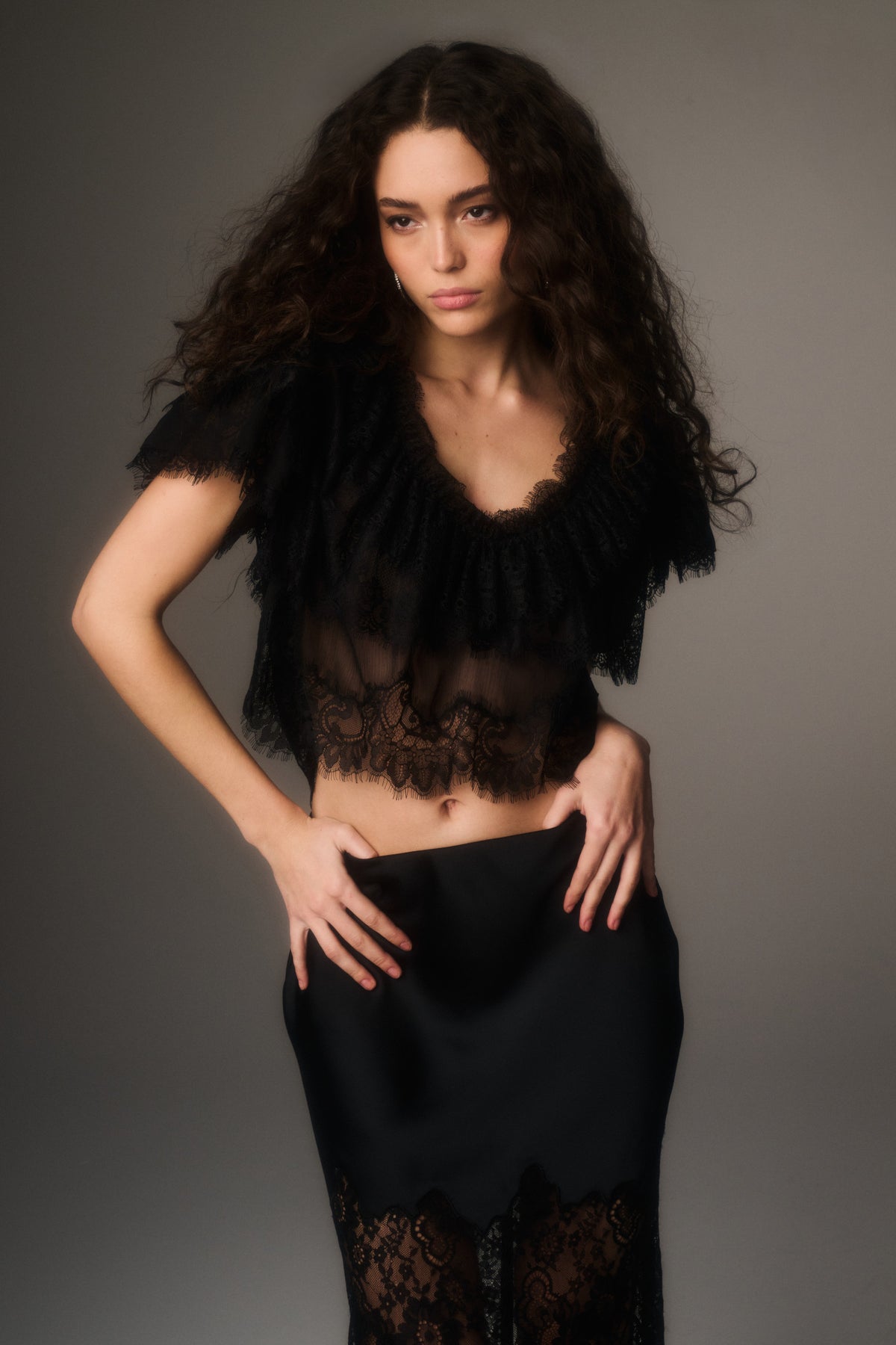 Black lace chiffon cropped top with scalloped V neckline and lace hem, model standing