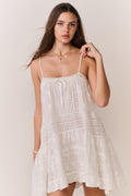 White cotton mini dress with lace pattern, thin straps, and tiered hem