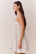 White lace mini dress with spaghetti straps, tiered skirt, and soft tassel detail