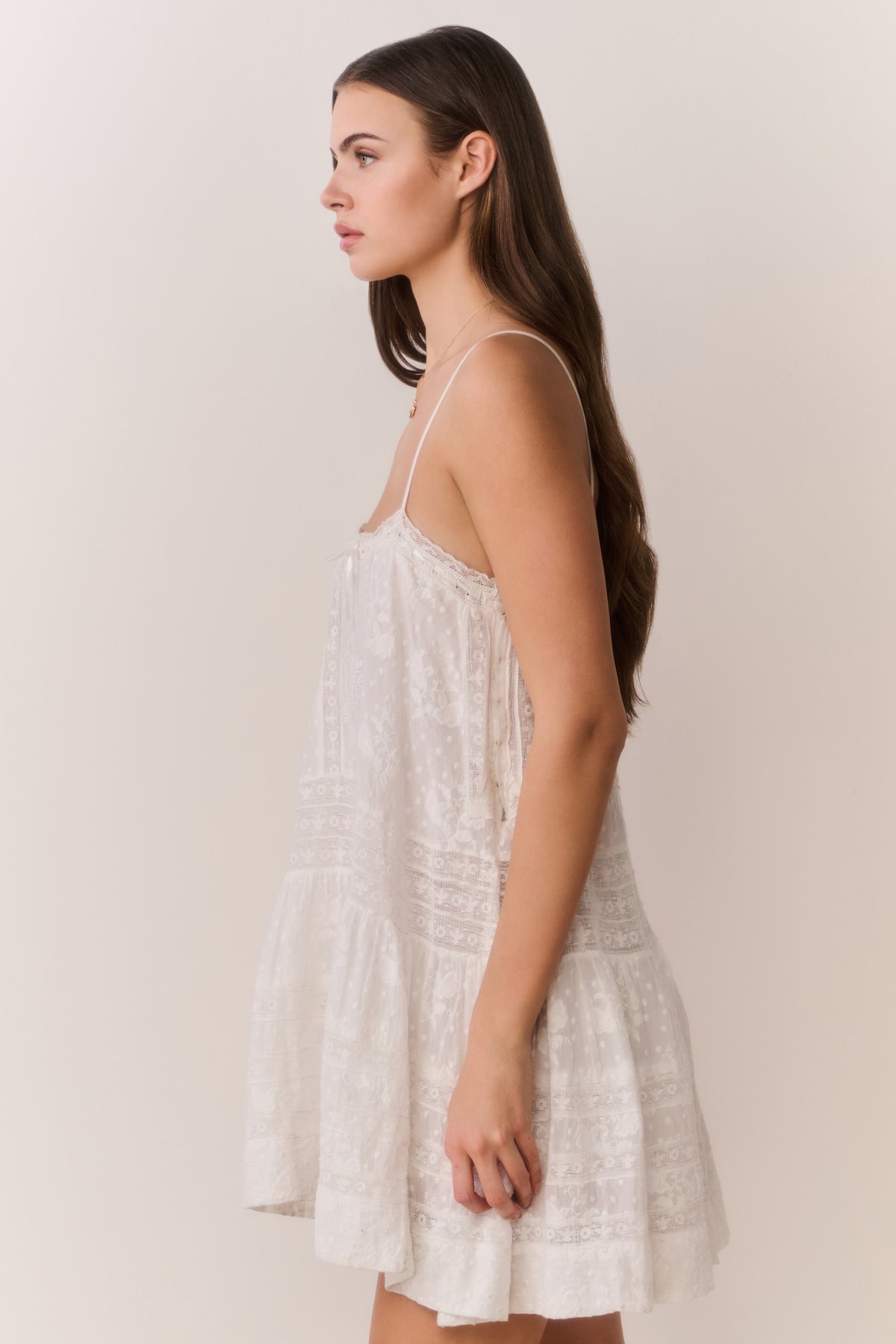 White lace mini dress with spaghetti straps, tiered skirt, and soft tassel detail