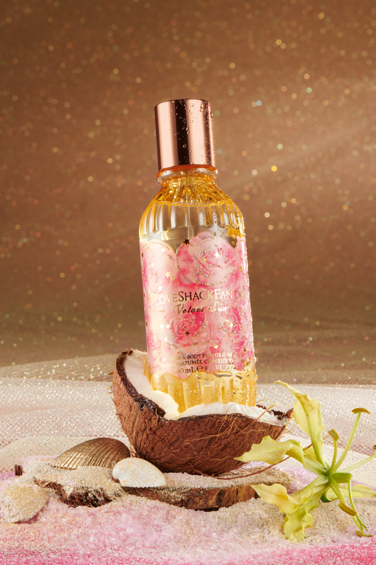Hair and body perfume mist bottle with gold liquid, metallic cap, and coconut pieces