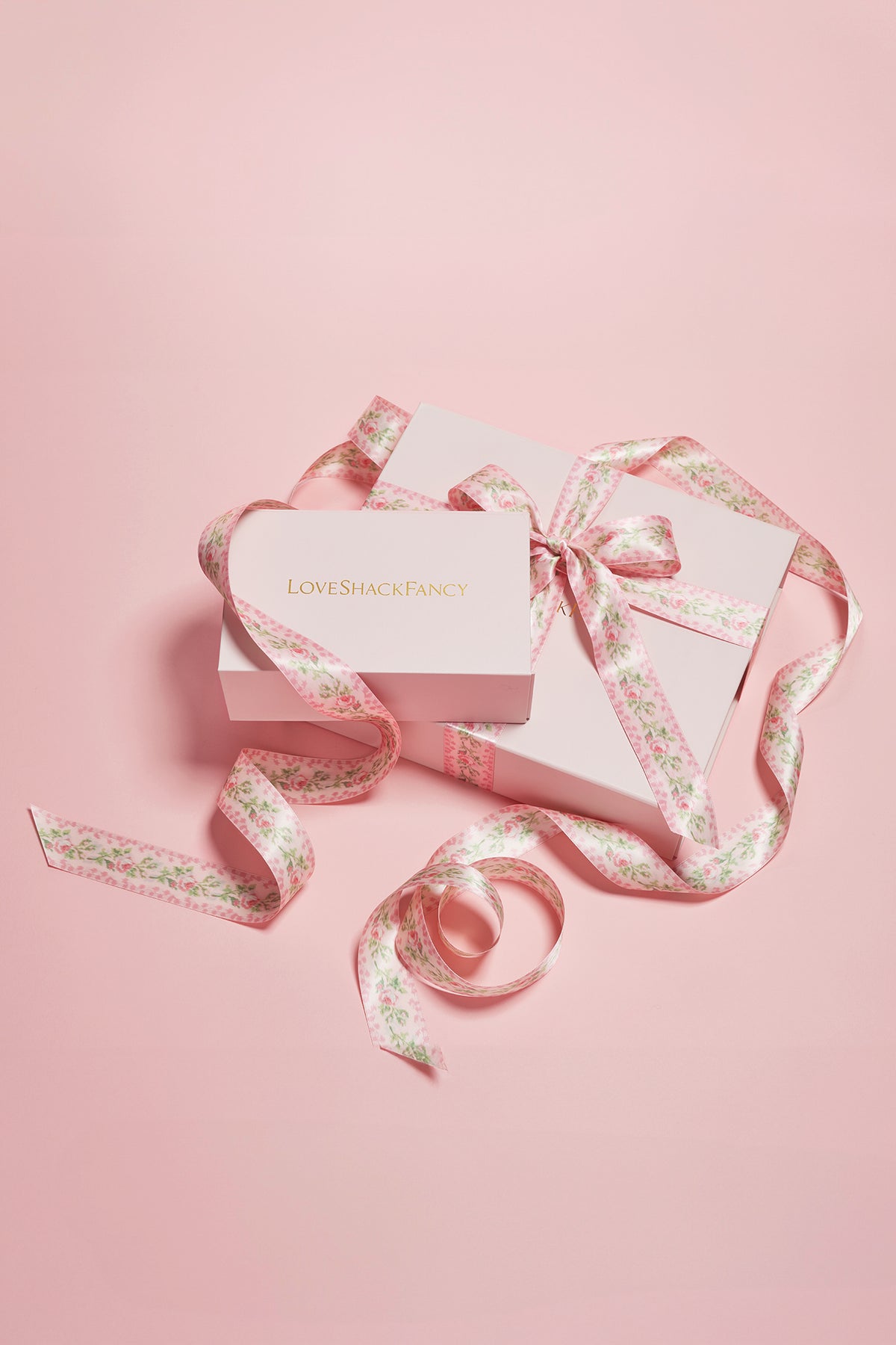 Pink gift packaging box with floral ribbon bow and loose ribbon tails
